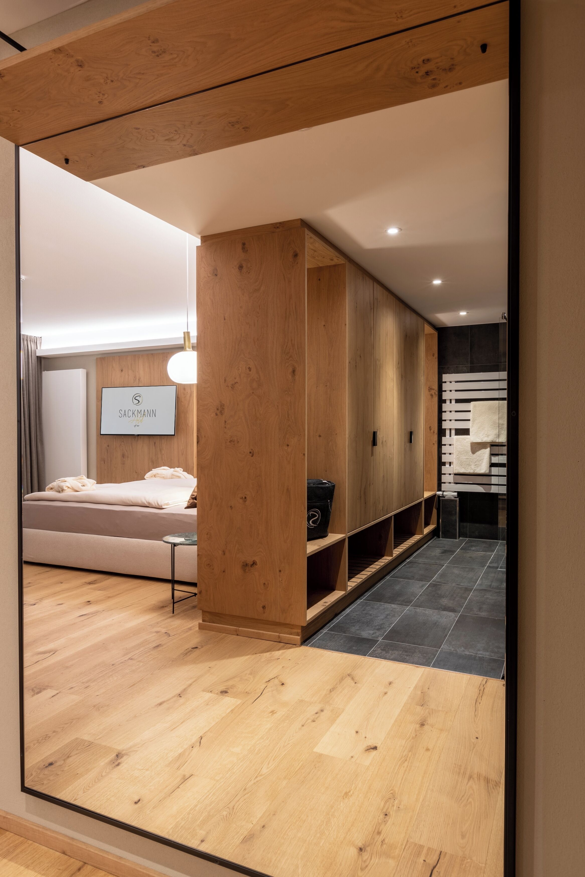 Ein modernes Hotelzimmer mit einem Holzschrank, einem Bett mit weißem Kopfteil und einer kleinen Sitzecke mit Tisch und Stühlen.
