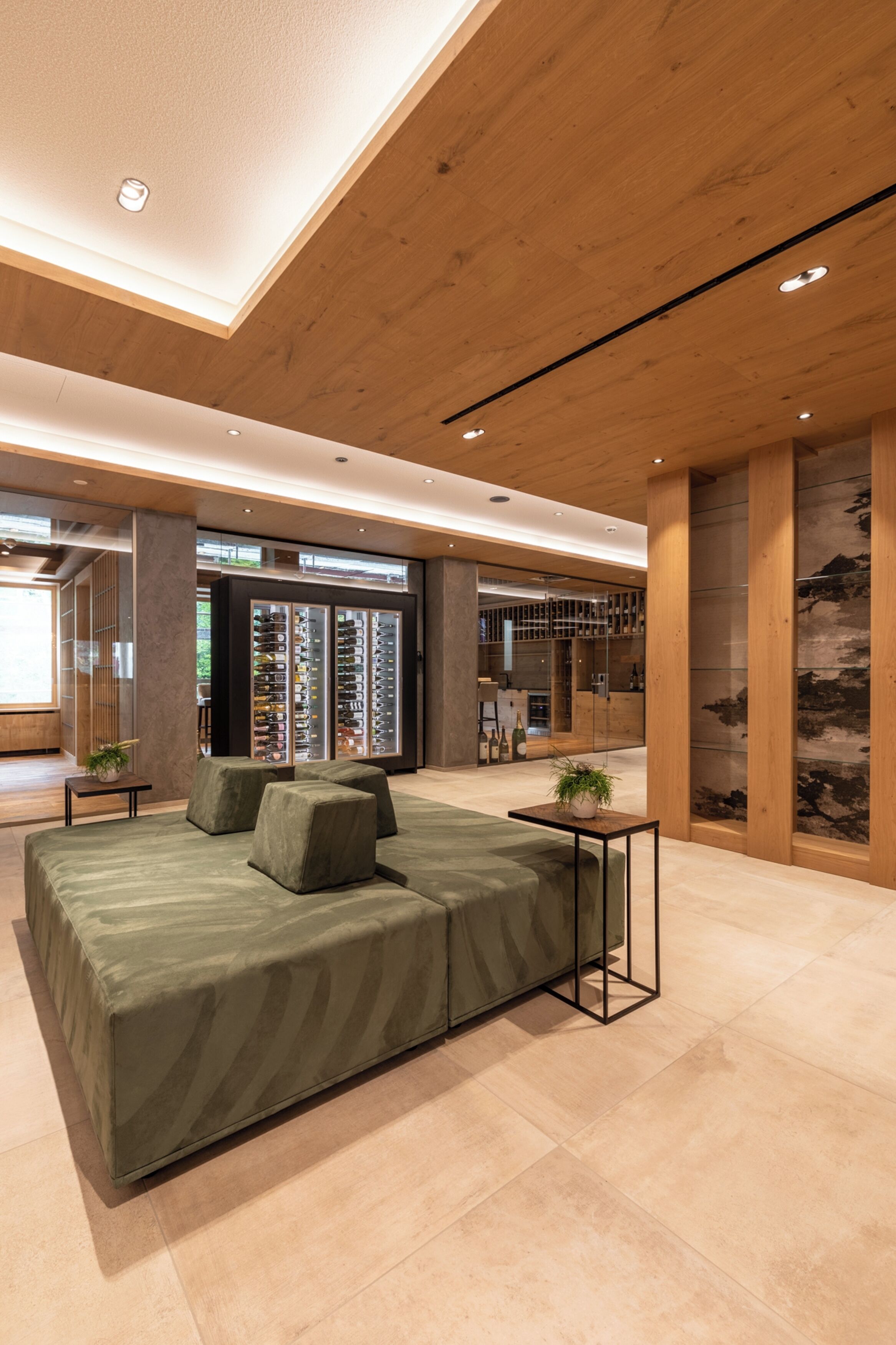 A modern hotel lobby with a large bed, a small table with a plant, and a wine refrigerator.