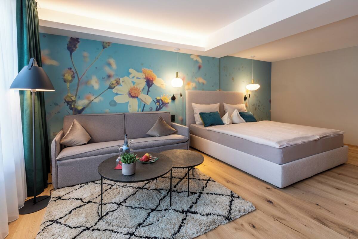 A modern bedroom with a sofa, a bed, a small table, and a decorative wall mural.