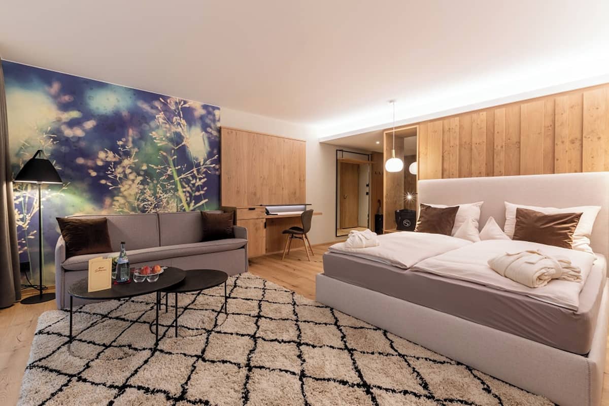 A modern hotel room with a large bed, a sofa, a desk, and a large floral artwork on the wall.