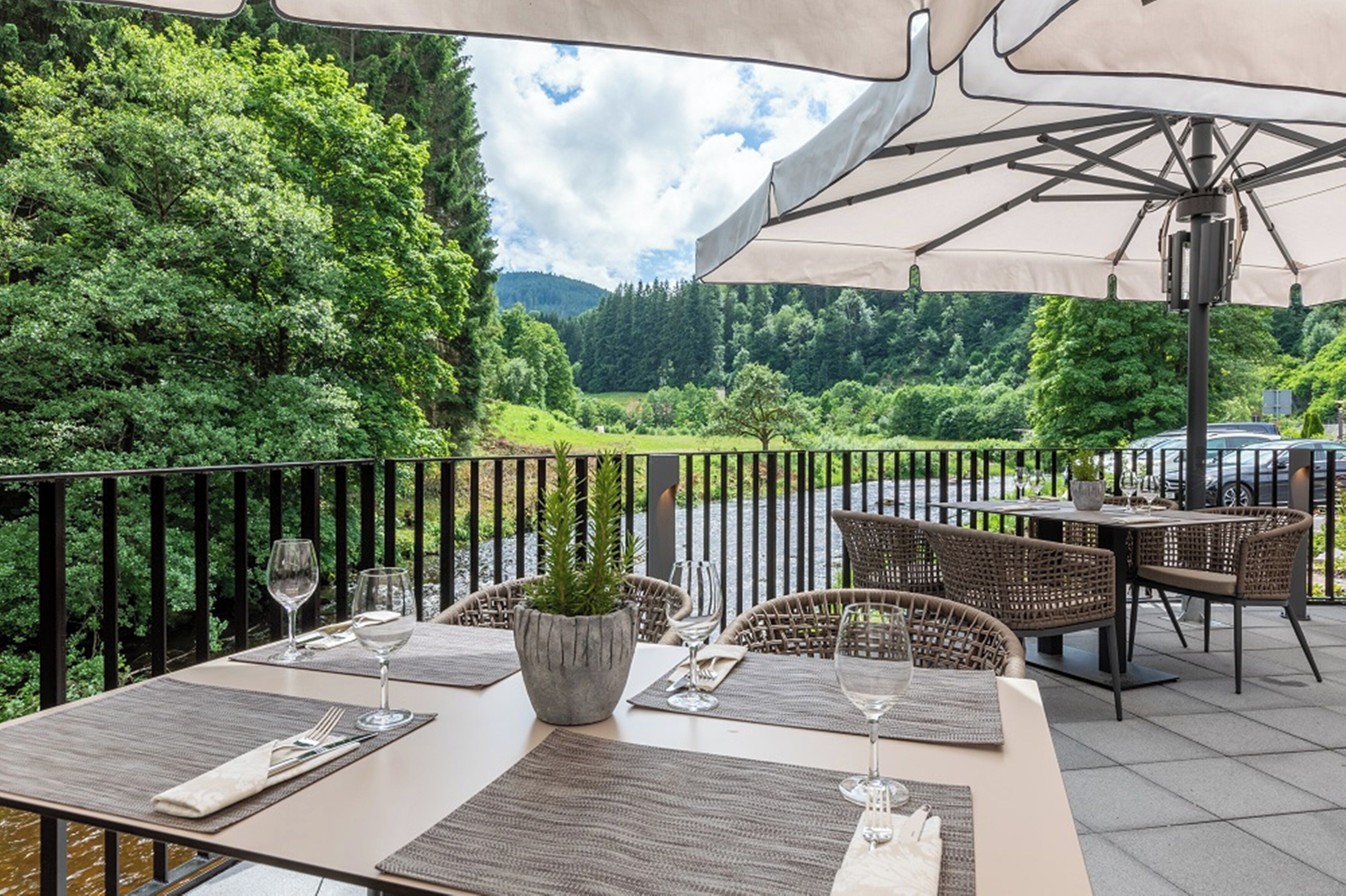 Een terras met tafels, stoelen en parasols, met uitzicht op een weelderig groonlandschap.