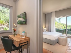 Un dormitorio con cama, escritorio y silla, ventana con vistas a zonas verdes, y un cuadro en la pared.