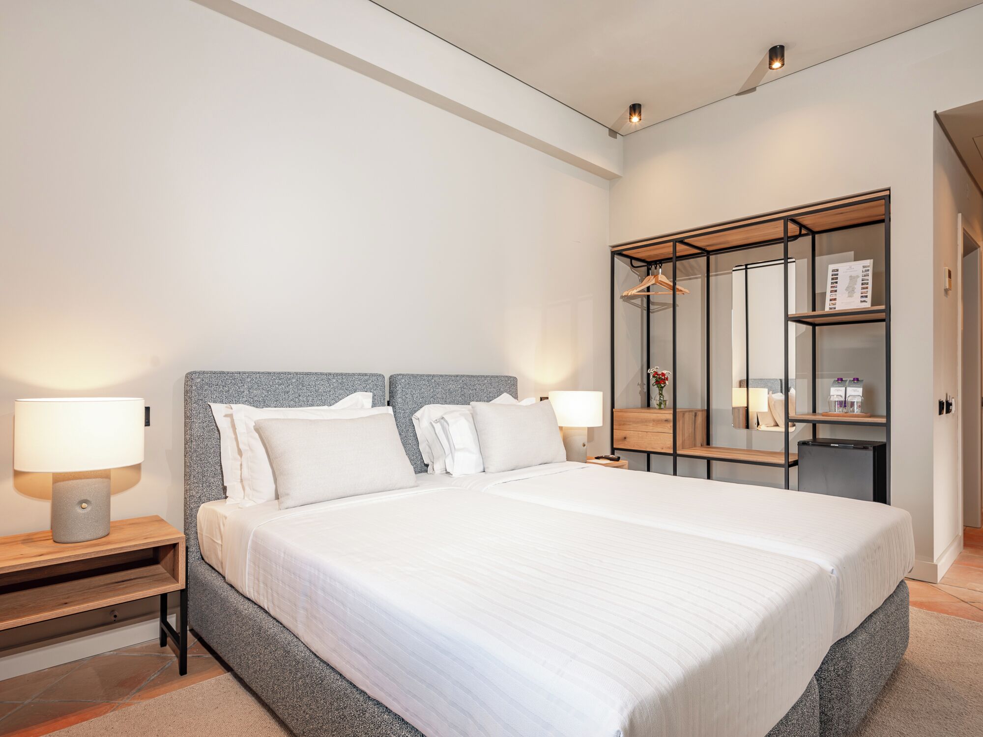 Ein modernes Hotelzimmer mit einem großen Bett, Nachttischlampen, einem Schrank mit Spiegel und einem kleinen Tisch.
