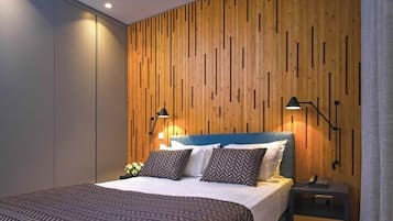 Quarto moderno com parede de painel de madeira, cama com roupa de cama estampada, duas luminárias de cabeceira e mesa de cabeceira com um telefone.