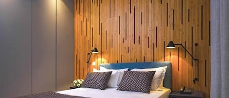 A modern bedroom with a wooden panel wall, a bed with patterned bedding, two bedside lamps, and a nightstand with a phone.