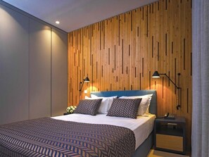 A modern bedroom with a wooden panel wall, a bed with patterned bedding, two bedside lamps, and a nightstand with a phone. - Caldas Monchique Villa Termal Spa Resort (Monchique)