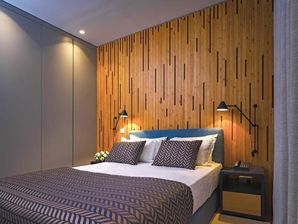 Un dormitorio moderno con un panel de madera en la pared, una cama con ropa de cama estampada, dos lámparas de noche y una mesita de noche con un teléfono.