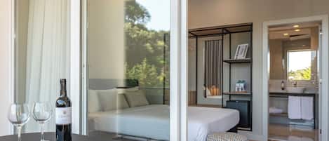 A modern hotel room with a bed, a bathroom, and a dining area with a table set with food and wine.