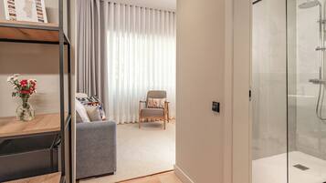 A modern bathroom with a glass shower enclosure, a wooden floor, and a seating area with a chair and cushions.