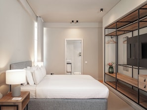 Quarto de hotel moderno com cama, luminária de cabeceira, televisão e guarda-roupa com espelho.