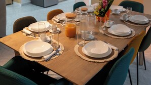Un coin repas avec une table en bois dressée pour quatre personnes, entourée de chaises de couleur turquoise, et une cuisine en arrière-plan.
