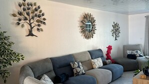 Un salon moderne avec un canapé d’angle, des œuvres d’art décoratives au mur et une plante en pot.