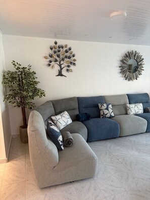 A living room with a sectional sofa, a potted plant, and wall art.
