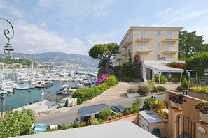 A coastal building with a marina view, a car, and a street with greenery.