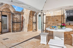 A stone patio with a white table and chairs, a metal gate, and a door.