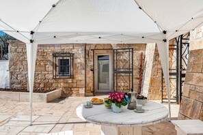 A stone building with a white door, a window, and a table with food and flowers under a white canopy.