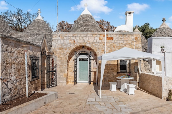 A stone building with a central archway, a white tent, and a small outdoor seating area.