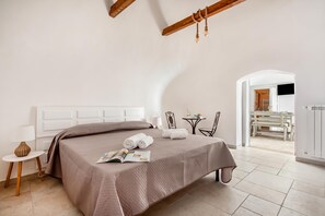 A bedroom with a bed, a side table, a lamp, and a view of a dining area.