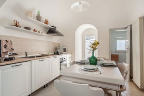 A modern kitchen with white cabinetry, a dining table set for four, and a view of the adjacent room through an archway.