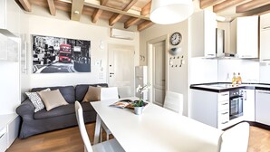 Una cucina moderna con mobili bianchi, forno a incasso e zona pranzo con tavolo bianco e divano grigio.