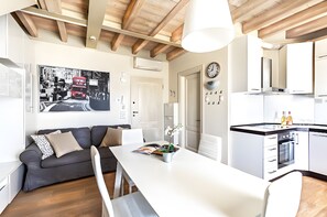 A modern kitchen with white cabinets, a built-in oven, and a dining area with a white table and grey sofa. - Apartment Chervo Golf Uno (Lombardia)