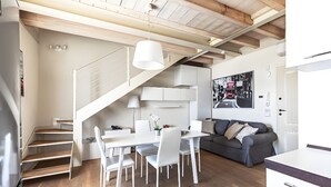 Una cucina moderna con mobili bianchi, un'area pranzo con sedie bianche, una scala e un divano grigio.
