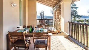 Zona pranzo all'aperto coperta con tavolo apparecchiato per due, sedie di legno e vista sul paesaggio.