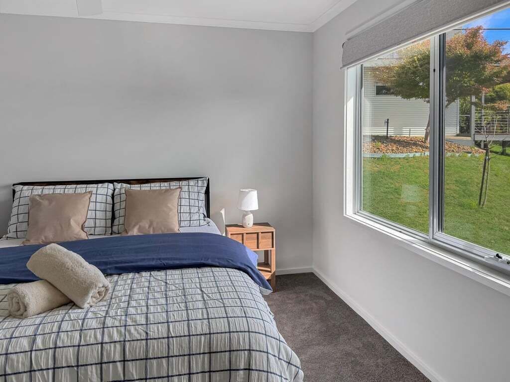 A bedroom with a bed, pillows, a nightstand, a lamp, and a window with a view of the outdoors.