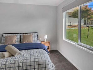 Una camera da letto con un letto, cuscini, un comodino, una lampada e una finestra con vista sull'esterno.