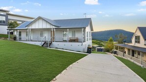 Uma casa moderna de dois andares com varanda coberta, escada visível e vista para a paisagem ao redor.