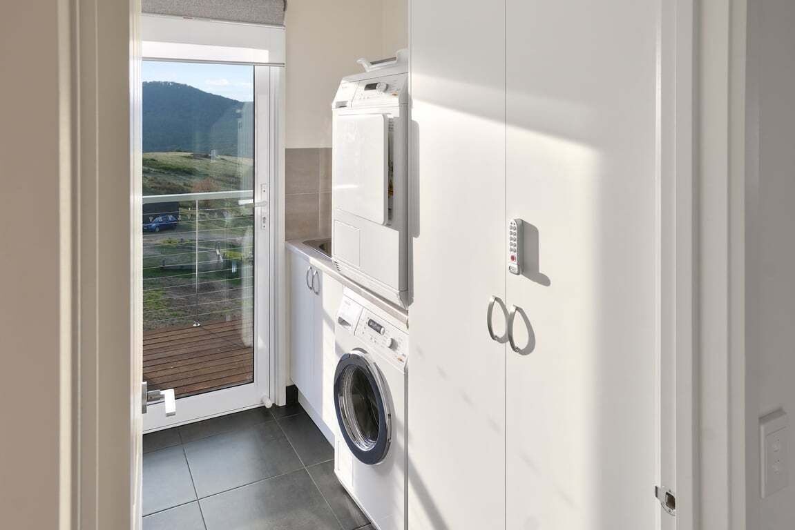 A laundry room with a washing machine and dryer, a door to a balcony, and a view of a hilly landscape.