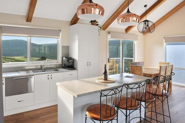 A modern kitchen with white cabinetry, a central island, and a dining area with metal chairs.