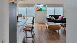 Um espaço interior com cozinha, área de refeições e sala de estar com sofá e televisão.