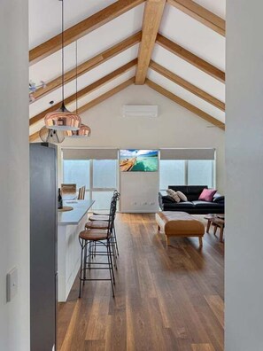 An interior with a kitchen area, dining space, and a living area with a couch and a TV. - Spotted Gum Merrijig (Mansfield)