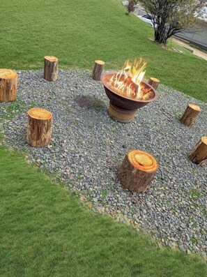 A fire pit surrounded by wooden stumps on a gravel area with grass around. - Spotted Gum Merrijig (Mansfield)