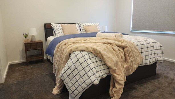 Quarto com cama, mesa de cabeceira, abajur e janela.