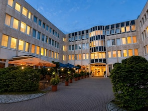Un pati d'hotel amb plantes en testos, mobiliari exterior i una entrada ben il·luminada.