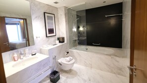 Ein modernes Badezimmer mit großem Spiegel, einer Badewanne, einer Toilette und einem Waschtisch mit Pflegeprodukten.