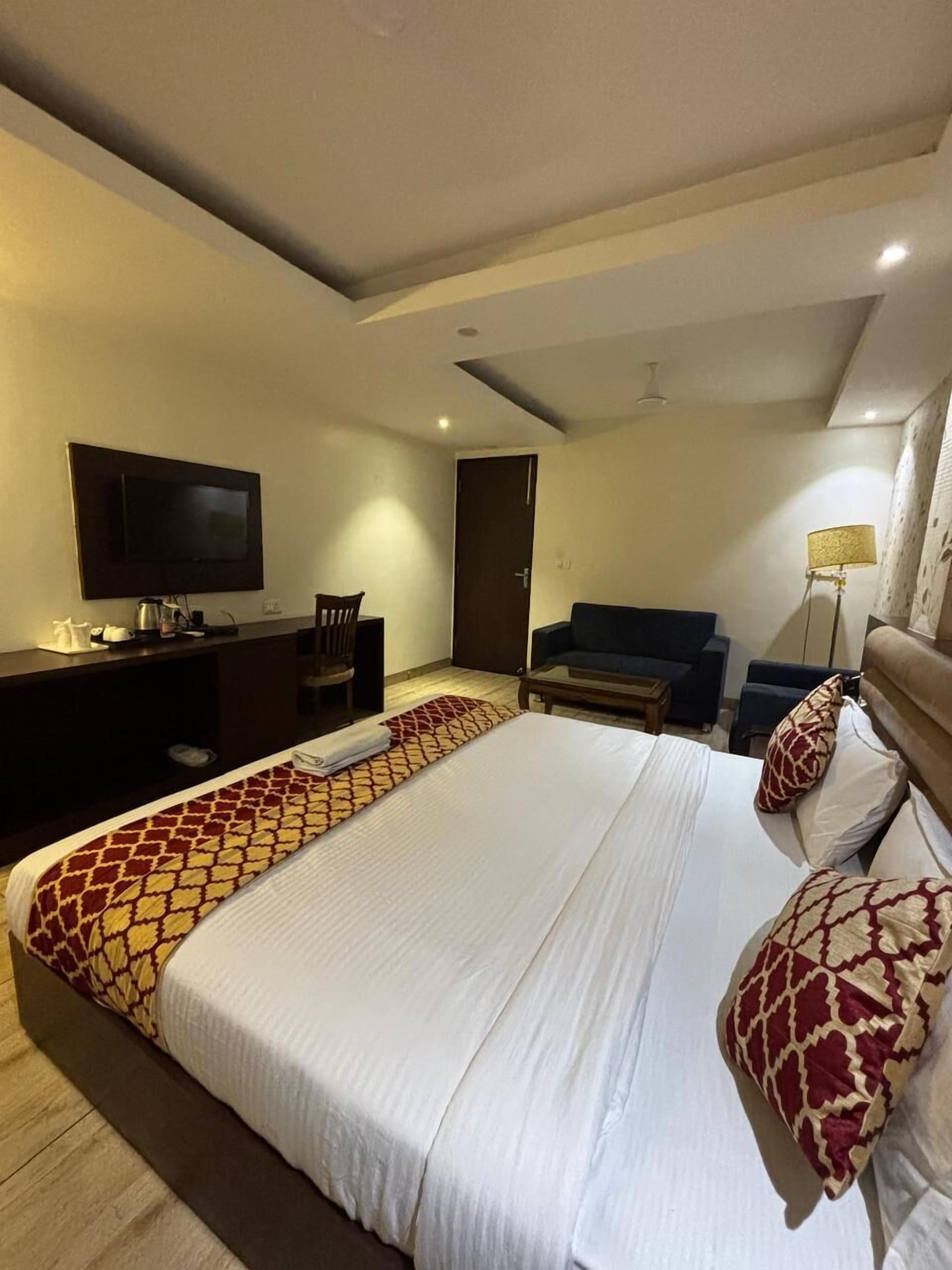 Habitación de hotel con una cama grande, un escritorio con televisor de pantalla plana, un sofá y una lámpara.