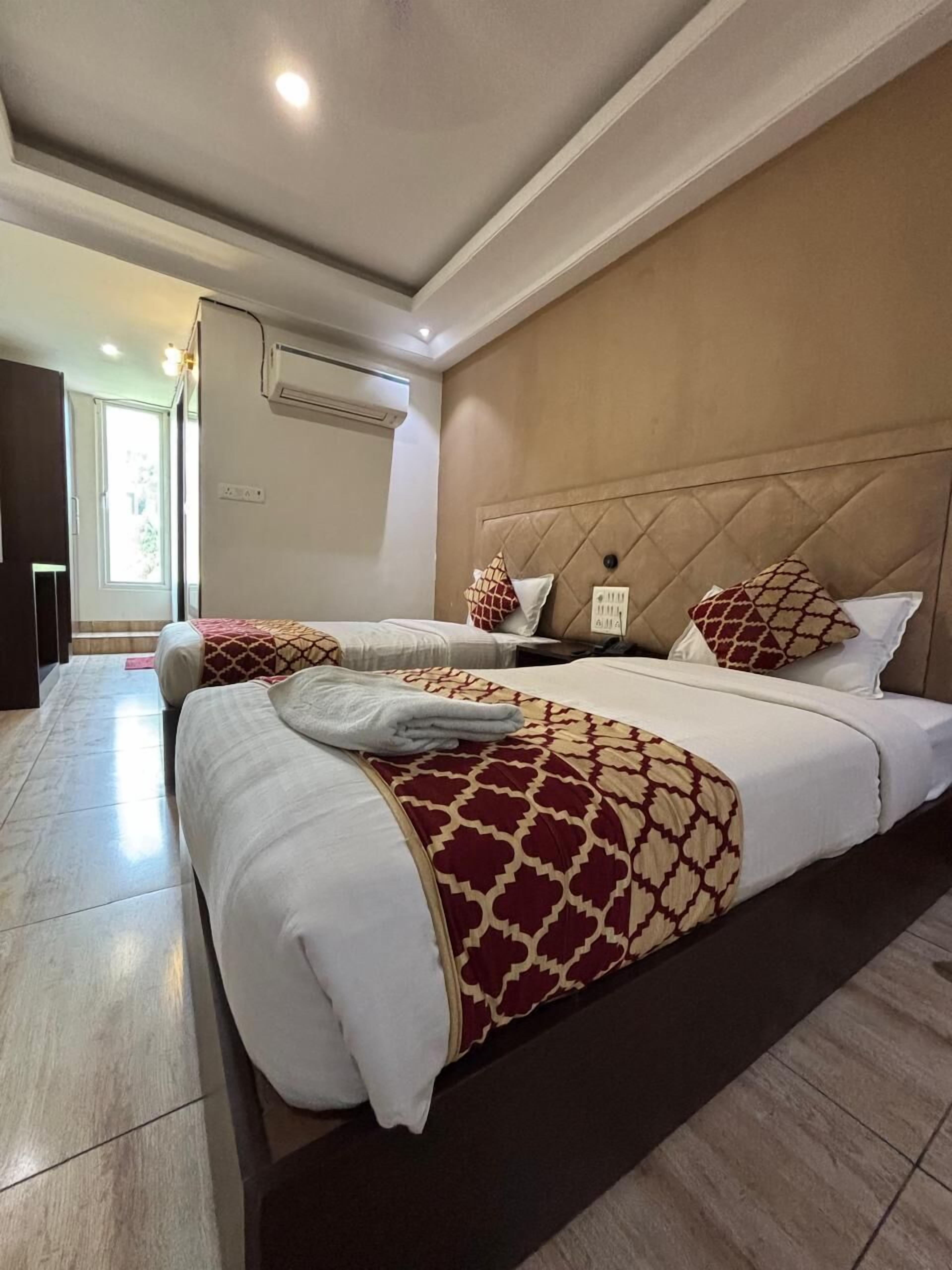A hotel room with two beds, a large window, a wall-mounted air conditioner, and a tiled floor.