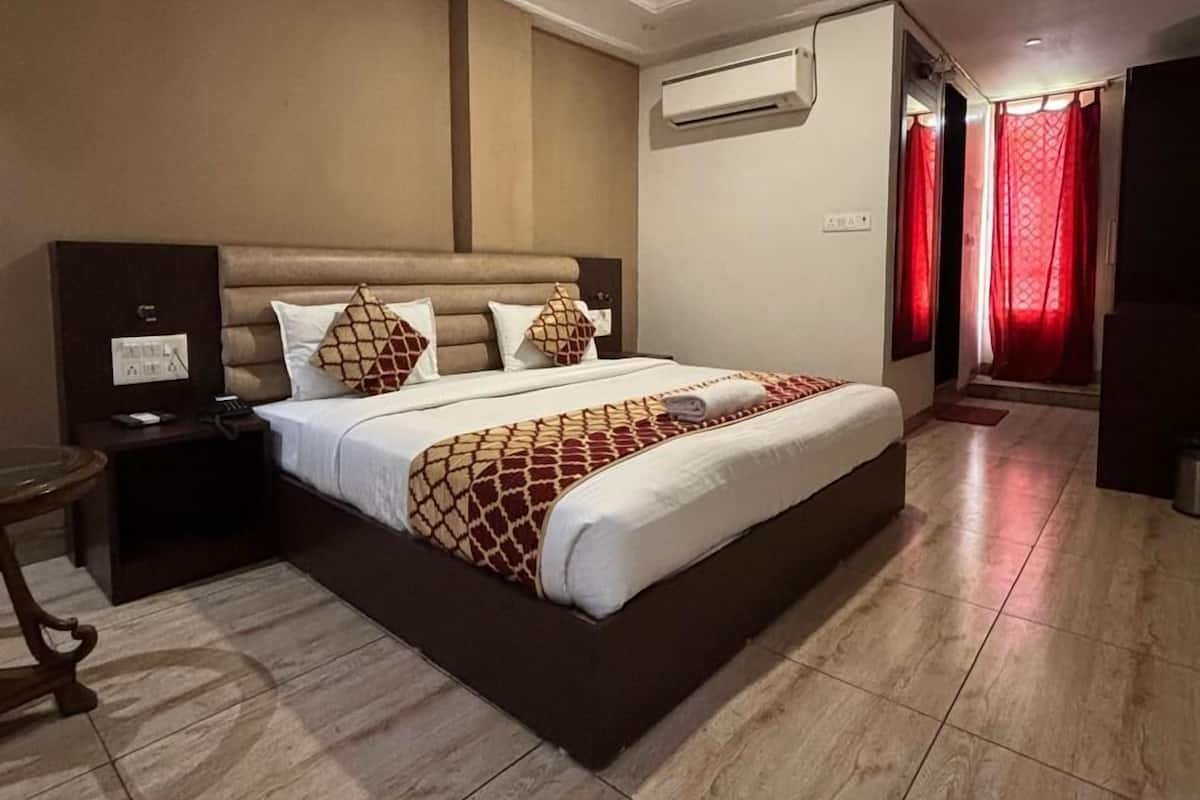 Una habitación de hotel con una cama grande, un aire acondicionado, una mesita de noche y una pequeña mesa.