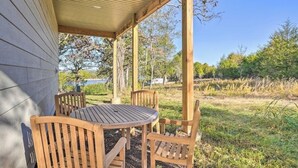 Ein überdachter Außenbereich mit Tisch und Stühlen, Holzbalken und Blick auf Bäume und ein Gewässer.