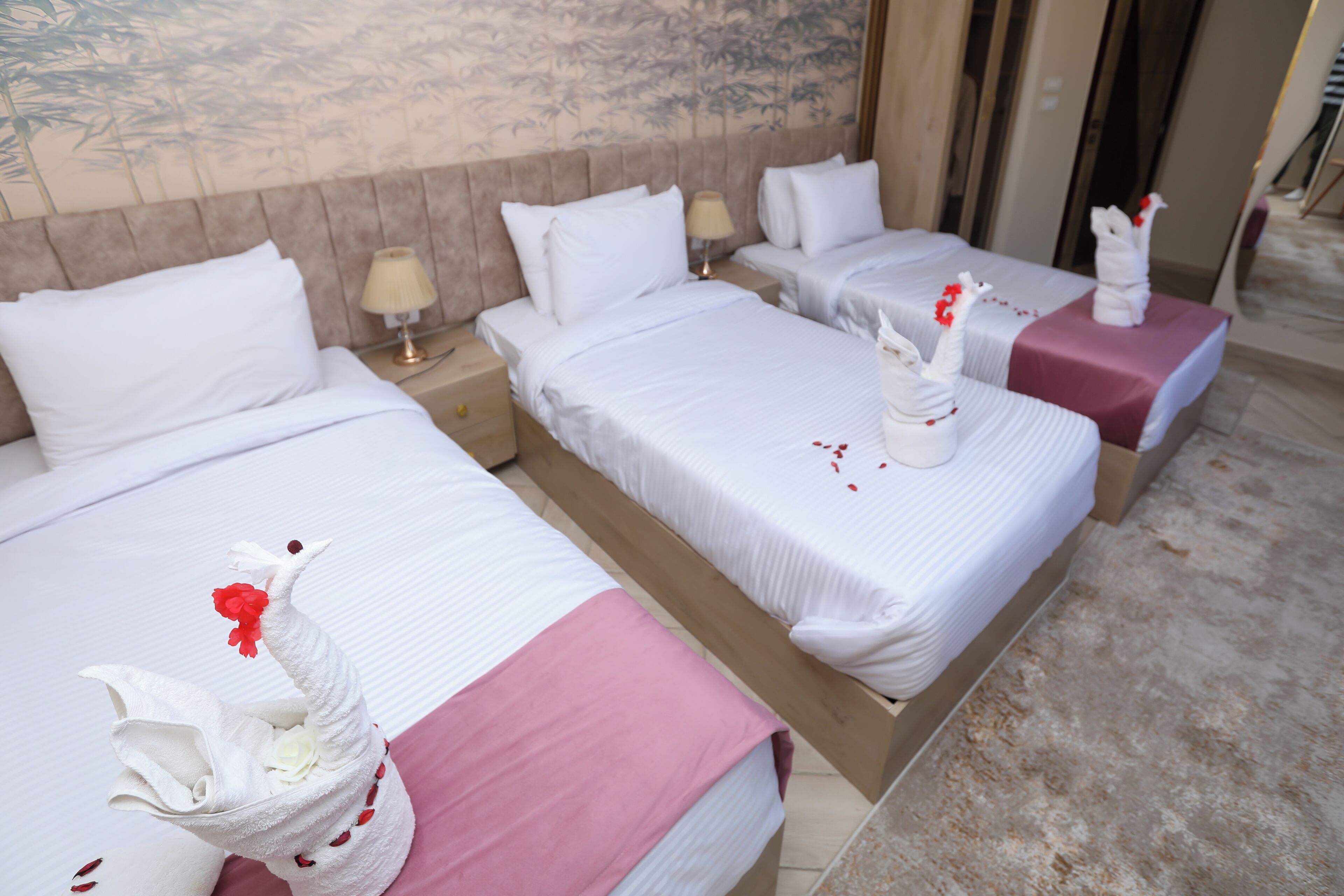 A hotel room with three beds, each with white bedding and pink accents, and decorative swan pillows.