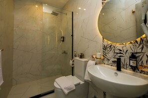 Un baño moderno con cabina de ducha de vidrio, inodoro blanco y un lavamanos grande con espejo superior.