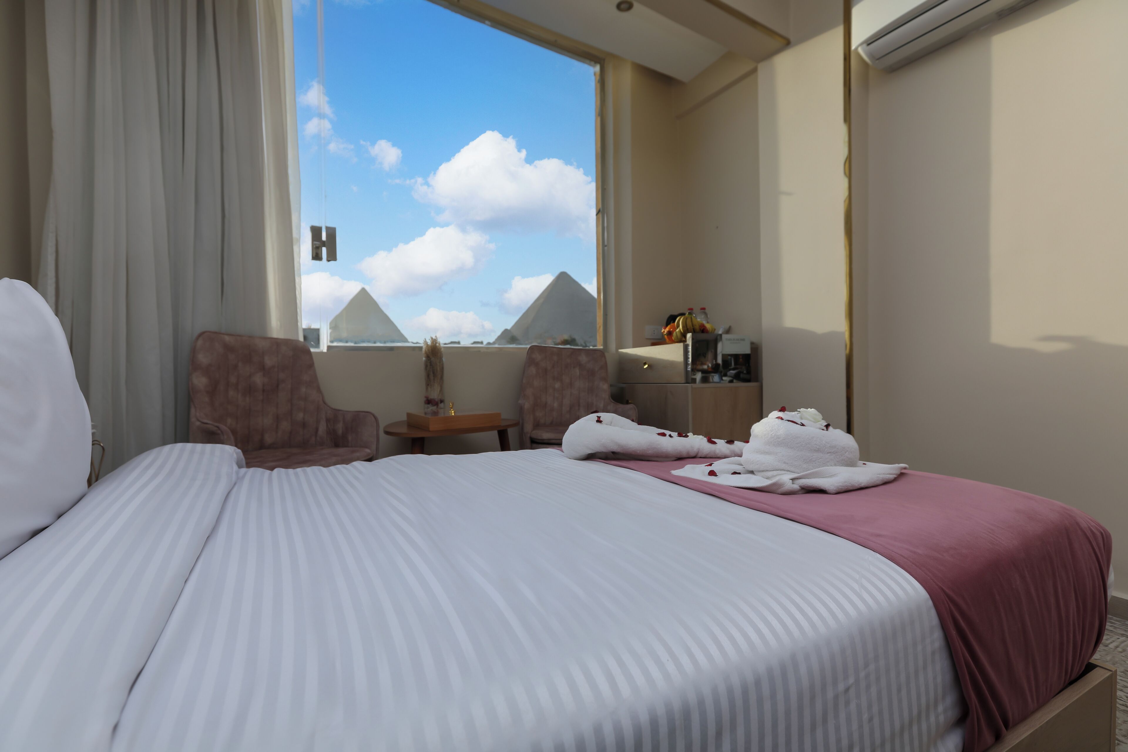 Habitación de hotel con cama, una silla, una mesita y vista a las pirámides.