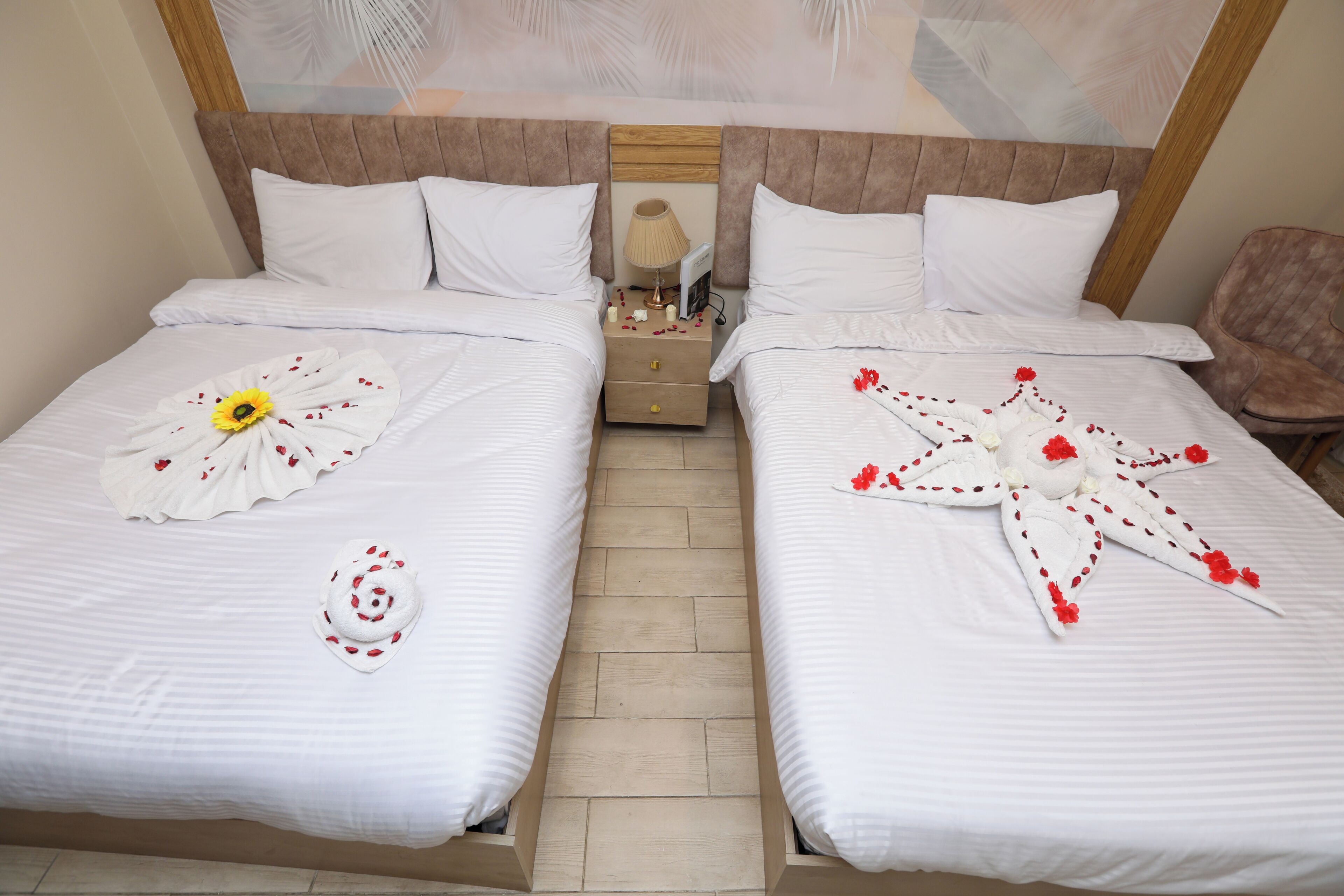 A double bed with white bedding and floral arrangements, a wooden headboard, a nightstand with a lamp, and a chair.