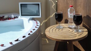 Una habitación con vista a una pirámide por la ventana, una bañera blanca con pétalos de rosa, dos copas de vino y una botella de agua sobre una mesa de madera.