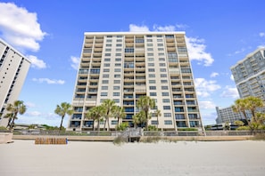 A multi-story hotel with balconies, a beach view, and palm trees. - Arcadian 1 | 2 Bedroom Oceanfront Condo (Myrtle Beach)