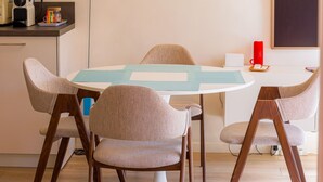 Zona pranzo con tavolo rotondo, quattro sedie, una lampada a sospensione blu, un punto luce a parete e un quadro incorniciato.
