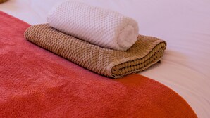 Un letto rifatto con lenzuola bianche, una coperta marrone e rossa e una lampada su un comodino.